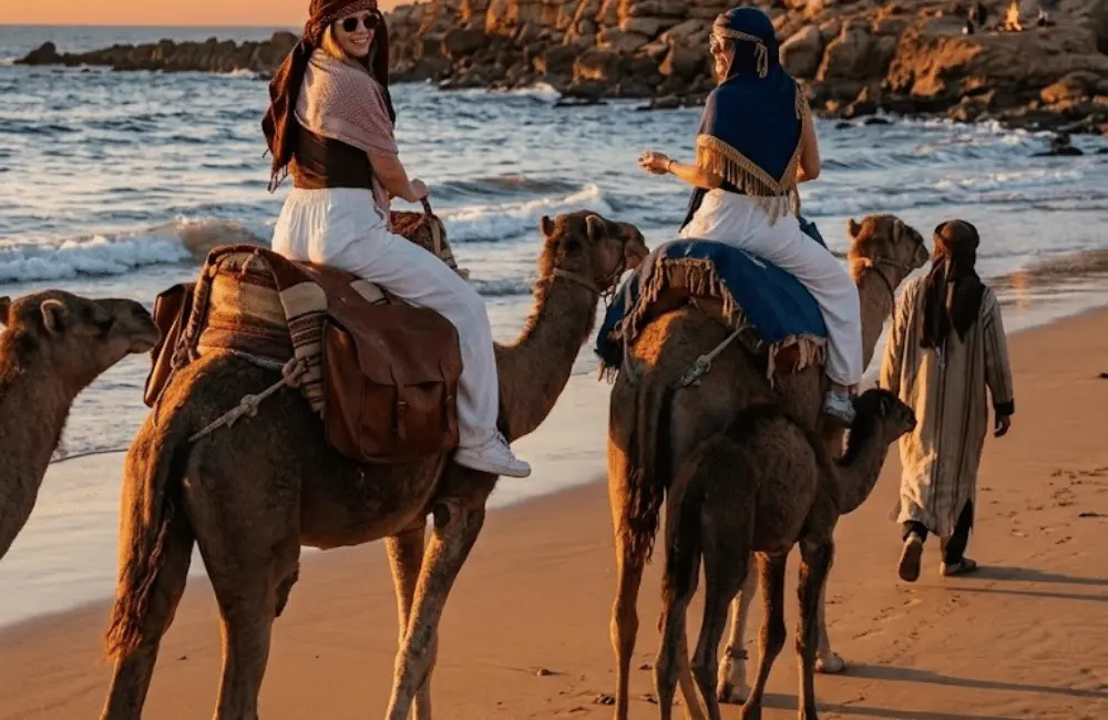Derniers rayons sur la plage Deux voyageuses en balade à dos de dromadaire au coucher du soleil à Essaouira