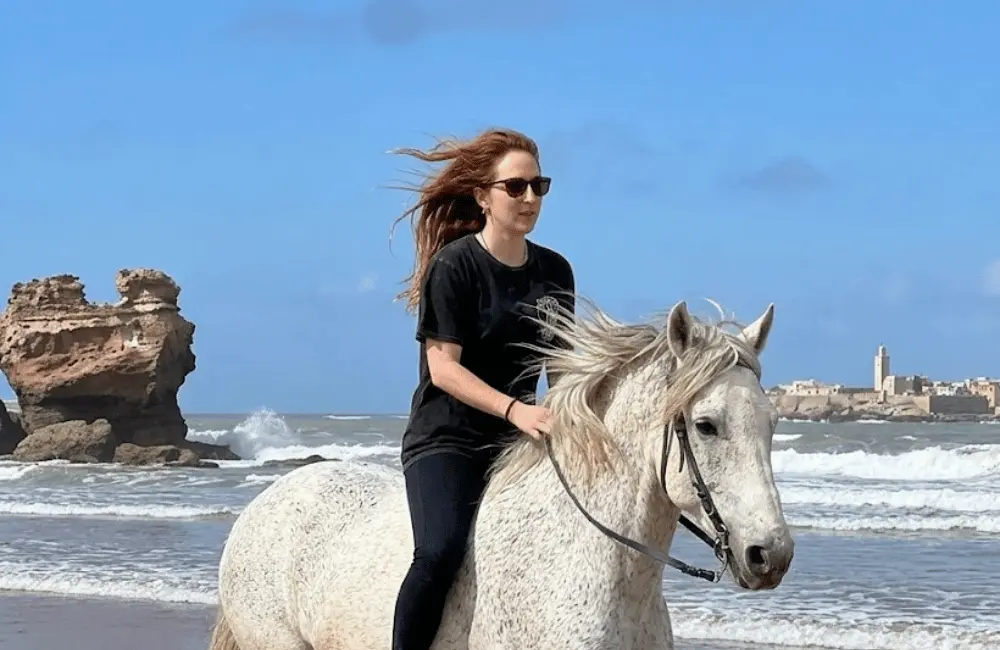 Deux cavaliers longeant la plage et le château de Barbe Noire à cheval à Essaouira