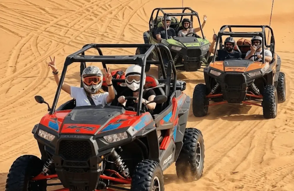 Trois buggys biplaces en convoi avec des participants casqués dans les dunes d’Essaouira