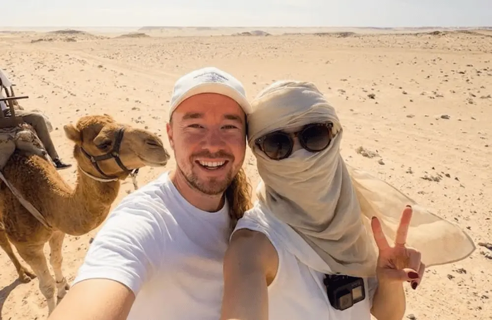 Un selfie avec la caravane Couple de voyageurs prend un selfie avec un dromadaire dans un paysage de sable